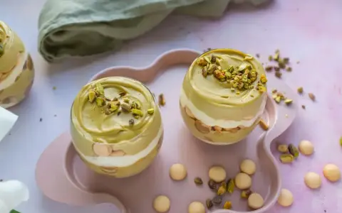 Dwa pucharki z kremem pistacjowym z mascarpone, udekorowane posiekanymi pistacjami.