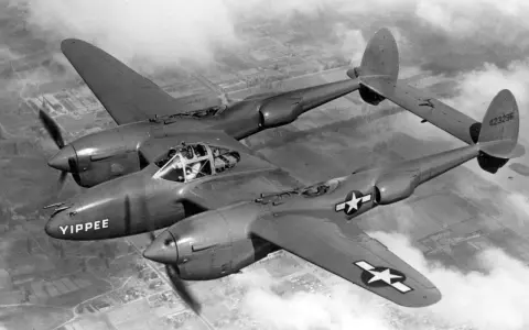 Ein P-38 Flugzeug mit dem Namen "YIPPEE" fliegt über Wolken.