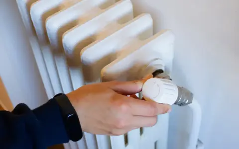 Mano ajustando el termostato de un radiador blanco. Controlar la temperatura ayuda a saber cuanto cuesta la calefaccion al mes.