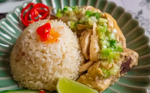 Un invitante piatto di riso con pollo, guarnito con cipollotti freschi, peperoncino rosso e una fetta di lime.