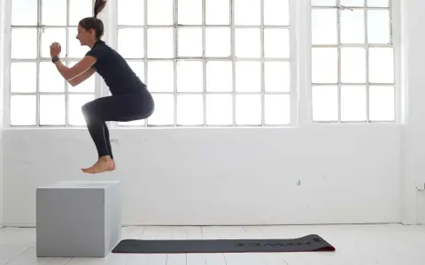 Frau macht **box jumps** in einem hellen Raum mit großen Fenstern.