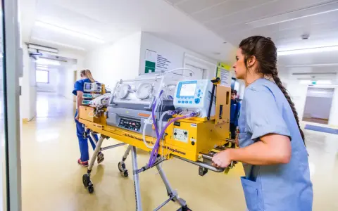 Infermiera spinge un'incubatrice mobile in un corridoio ospedaliero. Quanto tempo in terapia intensiva neonatale è cruciale per questi piccoli pazienti.