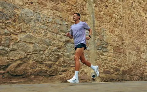 Uomo con tatuaggio corre lungo un muro di pietra. La sua tecnica di pronatore corsa è fluida e potente.