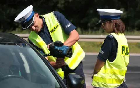 Policjanci w kamizelkach odblaskowych mierzą prędkość samochodu radarem.