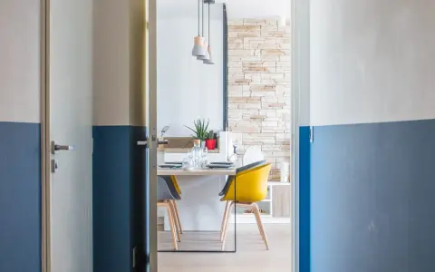 Peinture couloir 2 couleurs : un mur blanc cassé et bleu marine divise l'espace. Une porte s'ouvre sur une salle à manger moderne.