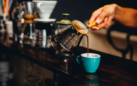 Ręka nalewa aromatyczną kawę z tygielka do turkusowej filiżanki. Idealny napój na pobudzenie przed treningiem.