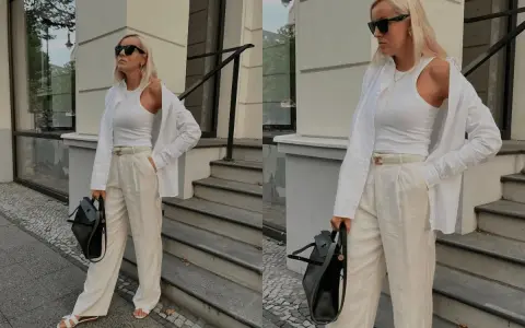 Eine Frau im Stil von quiet luxury, gekleidet in weiße Kleidung, steht vor einer Treppe.