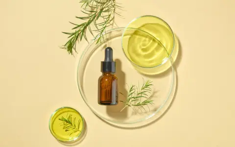 Flacone ambrato con contagocce, oli essenziali e rametti verdi su vetrini da laboratorio. Attenzione: il tea tree oil brucia la pelle se non diluito.