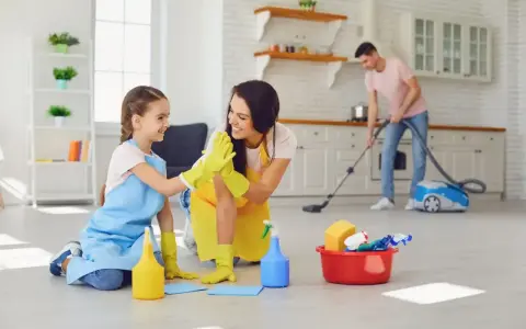 Mama i córka świętują udane porządki. W tle tata odkurza. To świetny przykład, jak obowiązki 9 latka w domu mogą być wspólną zabawą.