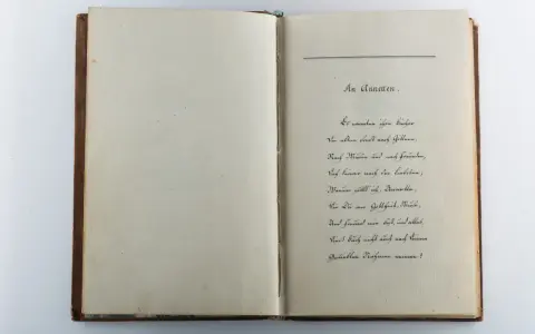 Ein aufgeschlagenes Buch mit handschriftlichem Gedicht auf der rechten Seite.