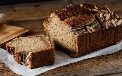 Un delicioso bizcocho de plátano, con almendras laminadas en la parte superior y una rebanada ya cortada, listo para disfrutar.