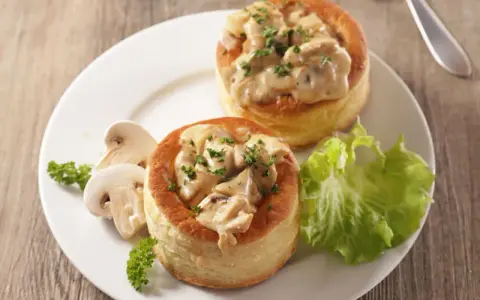Deux bouchées à la reine garnies d'une sauce crémeuse aux champignons, accompagnées de champignons frais et d'une feuille de laitue.