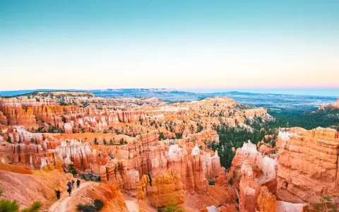 Zachód słońca nad Bryce National Park. Wąwóz pełen pomarańczowych hoodoos i zielonych drzew, z turystami na szlaku.