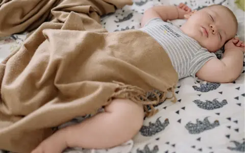 Bebé durmiendo plácidamente, envuelto en una manta de tonos tierra. Las medidas del arrullo bebé son ideales para su comodidad.