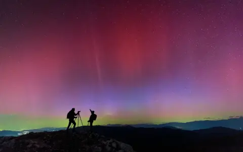Due fotografi ammirano l'incredibile aurora boreale in Italia, con sfumature rosa e viola che danzano nel cielo stellato.