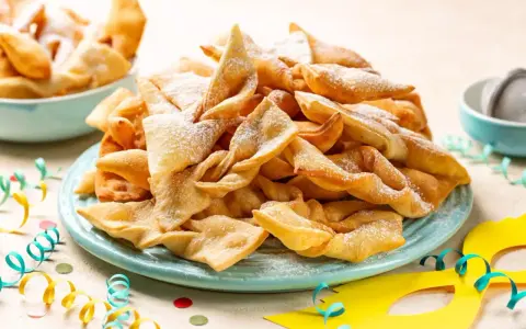 Un piatto colmo di chiacchiere, dolci tipici di Carnevale, cosparse di zucchero a velo. Festa e gusto, ecco cosa si mangia a Carnevale!