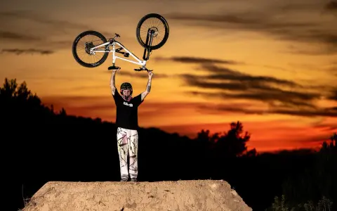 Tomas Lemoine triumphantly raises his bike against a fiery sunset, a champion on the dirt jump.