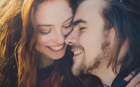 Uśmiechnięta para, jakby bliźnięta, w blasku słońca. Ich twarze blisko siebie, emanują radością i harmonią, niczym idealna waga.