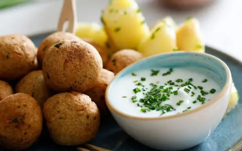 Polpette di ceci dorate e croccanti, servite con patate novelle e una ciotola di salsa cremosa guarnita con erba cipollina.