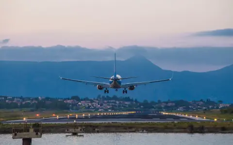 Ett flygplan landar vid Korfu flygplats i skymningen. Landningsbanans ljus lyser upp vägen.