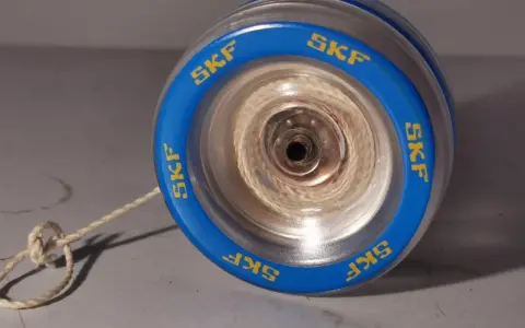 Blå jojo med kullager och texten "SKF" runt kanten. Snöret är knutet och ligger på ett grått underlag.