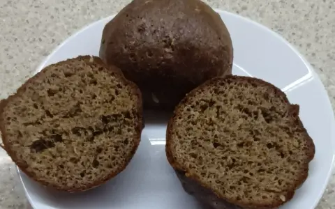 Na talerzu leżą keto bułki babka jajowata. Jedna jest cała, dwie pozostałe przekrojone na pół, ukazując puszyste wnętrze.