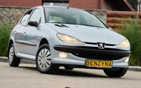 Jasny Peugeot 206 1.4 benzyna z żółtą tablicą "BENZYNA" na zderzaku, zaparkowany na zewnątrz.