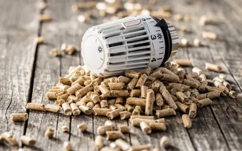 Ein Thermostat auf einem Haufen Holzpellets. Die Frage "wie lange heizt man mit 1 tonne pellets" wird hier visuell thematisiert.