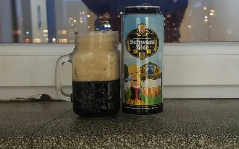 Perlenbacher Schwarz Bier w kuflu, obok puszka piwa. Wieczorny widok na miasto w tle.