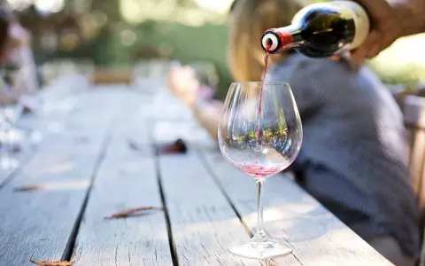 Czerwone wino nalewane z butelki do kieliszka na drewnianym stole.