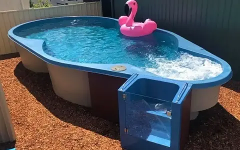 Petit jardin avec aménagement abord piscine hors sol. Un flamant rose gonflable flotte sur l'eau bleue.