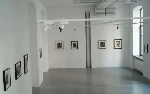 Galeria sztuki z pracami Karola Hillera. Wnętrze z białymi ścianami, szarą podłogą i kilkoma czarno-białymi fotografiami na ścianach.