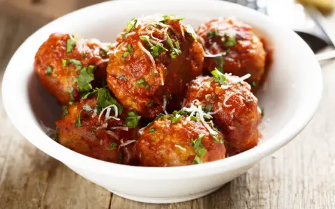 Polpette di carne morbide in salsa rossa, cosparse di parmigiano e prezzemolo fresco.