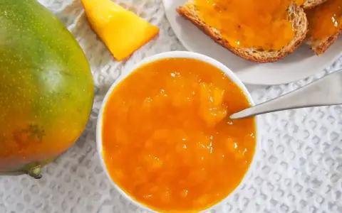 Słoik z dżemem z mango, obok świeży owoc i kromki chleba. Codzienne jedzenie mango to pyszny początek dnia.