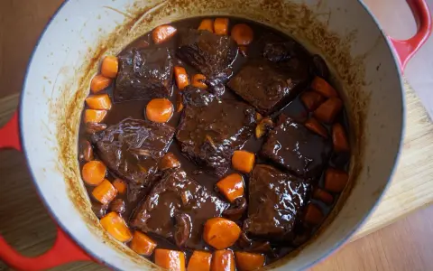 Boeuf bourguignon casero en olla roja, con trozos de carne tierna, zanahorias y champiñones en una rica salsa.