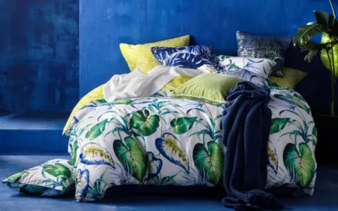 Ein tropisch gemustertes Bett mit Kissen in Blau und Grün. Für ein frisches Gefühl: wie oft Bettdecke wechseln?