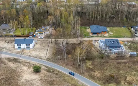 Widok z lotu ptaka na budowę domów jednorodzinnych, tworzących nowy plan ogólny gminy. Widać domy w różnym stanie budowy i drogę.