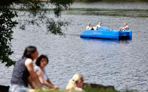 Sommerliche Ausblicke rund um Heiligenhaus: Menschen genießen den Tag am See, während drei Männer in einem blauen Tretboot über das Wasser gleiten.