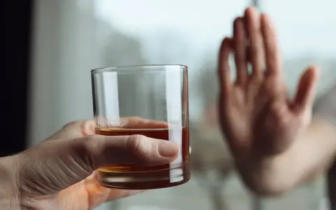 Dłoń odrzuca szklankę z alkoholem, symbolizując koniec z nałogiem i wyciek z wszywki.