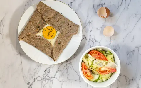 Une délicieuse crêpe complète bretonne avec un œuf coulant, accompagnée d'une salade fraîche.
