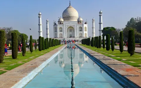 Majestatyczny Taj Mahal w Indiach odbija się w spokojnej wodzie, otoczony zielonymi ogrodami i strzelistymi cyprysami.