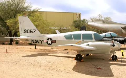 Ein zweimotoriges Piper-Flugzeug der US Navy mit der Kennung 9067 steht auf einem staubigen Flugplatz.