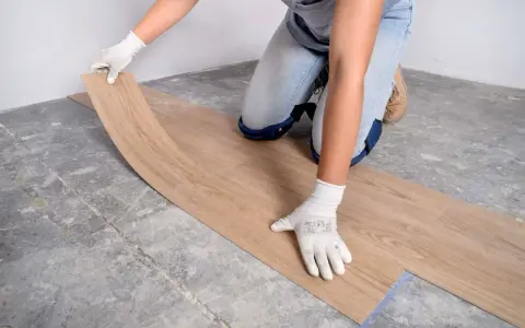 Manos enguantadas colocando suelo vinílico imitación madera sobre suelo de cemento.