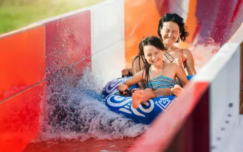 Mama i córka z uśmiechem zjeżdżają na pontonie po zjeżdżalni wodnej. Włochy ciekawostki dla dzieci: zabawa w aquaparku to świetny pomysł na wakacje!