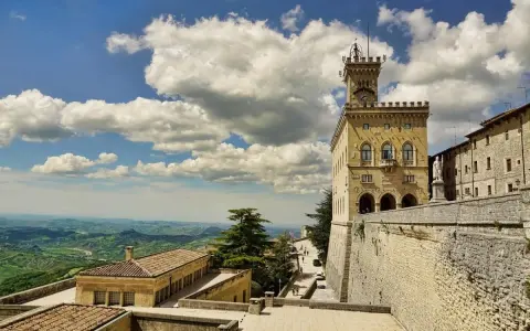 Torre del Campanone e Palazzo Pubblico nel **San Marino centro**, con vista panoramica sulle colline verdi sotto un cielo azzurro e nuvoloso.