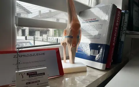 Model stawu kolanowego obok zaproszenia na terapię od Bartłomieja Kozłowskiego i książek o fizjoterapii.