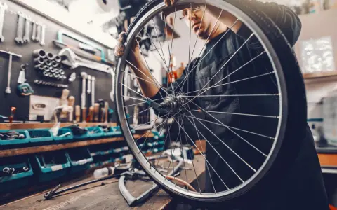 Mechanik sprawdza układy w rowerze, trzymając koło. W tle warsztat z narzędziami.