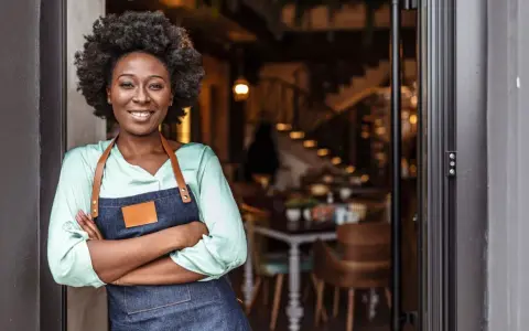 Mujer sonriente con delantal, lista para abrir su restaurante. Su plan de negocio es sólido.
