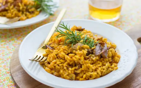 Delicioso arroz con setas y carne, servido en plato blanco con tenedor dorado y ramita de romero.