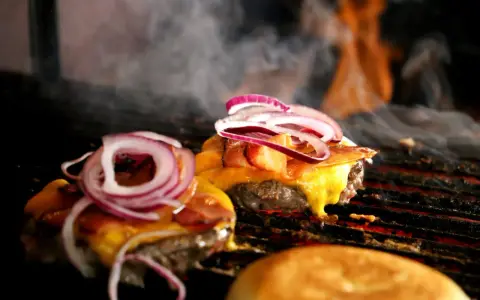 Pyszne burgery z grilla, z rozpływającym się serem i chrupiącym boczkiem, unoszą się w dymie.